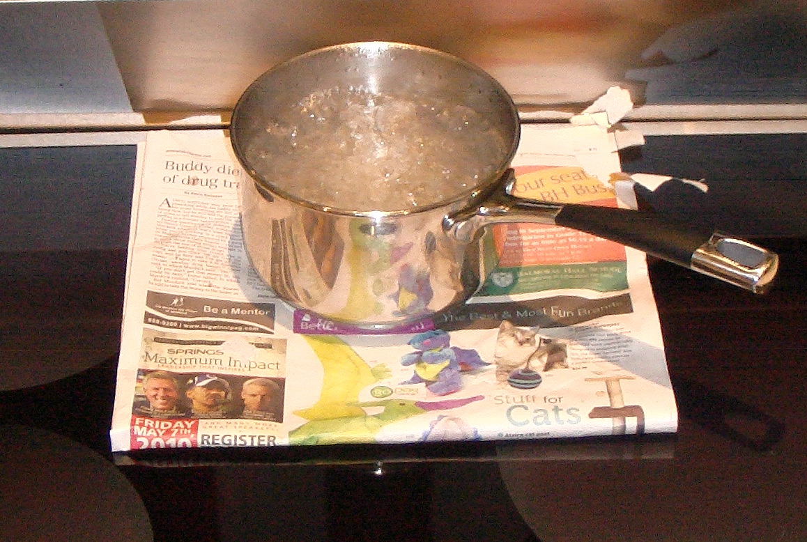 A pan of water boiling on an induction hob, with newspaper under it that stays cool
