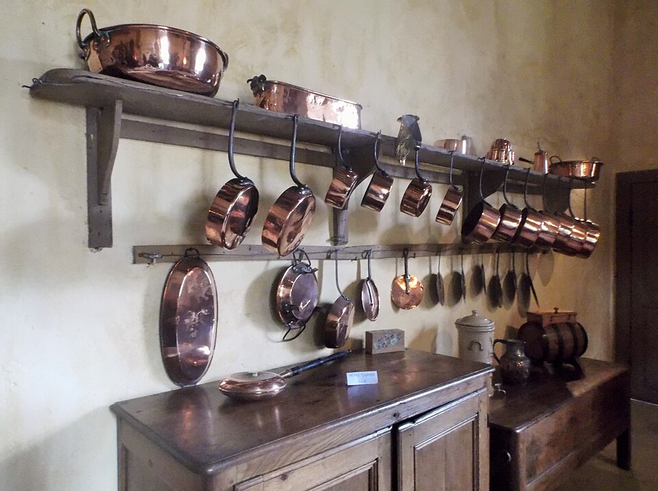 Copper pans hanging from a wall rail in a historic kitchen