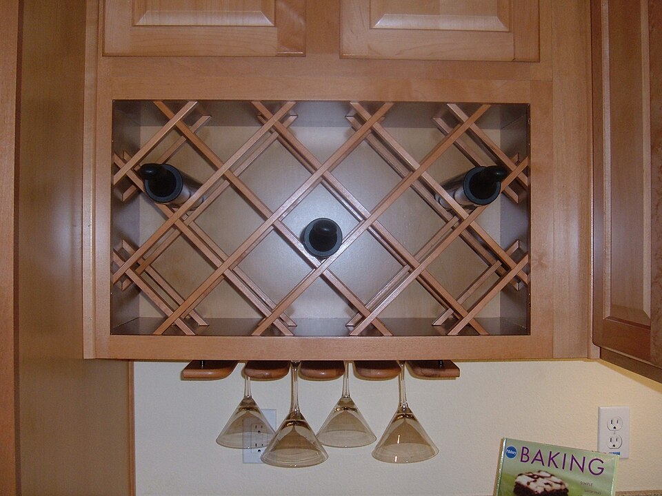 A lattice wine rack built into kitchen cabinets, with glasses hanging below