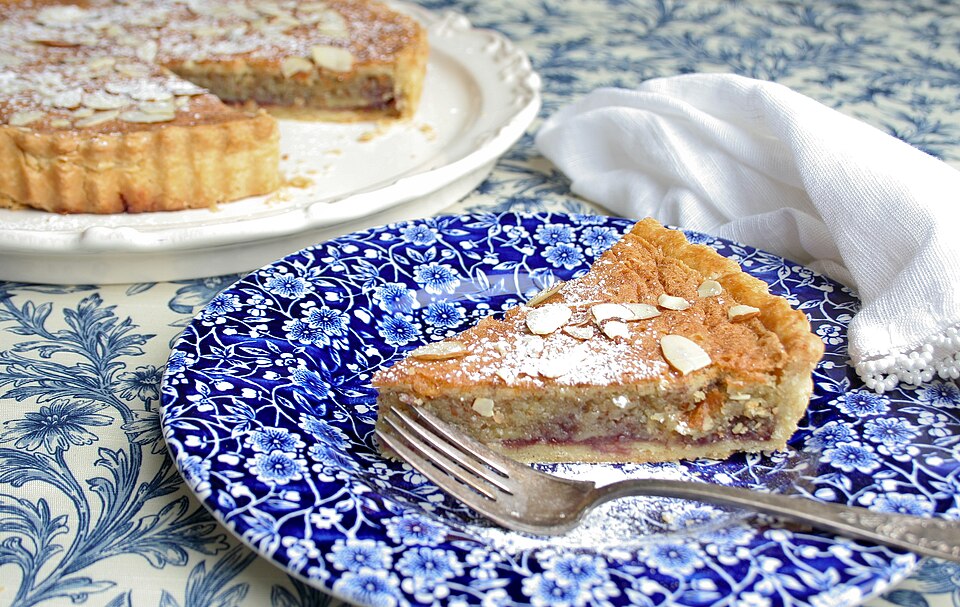 A Bakewell tart with a slice cut, showing the jam and almond filling