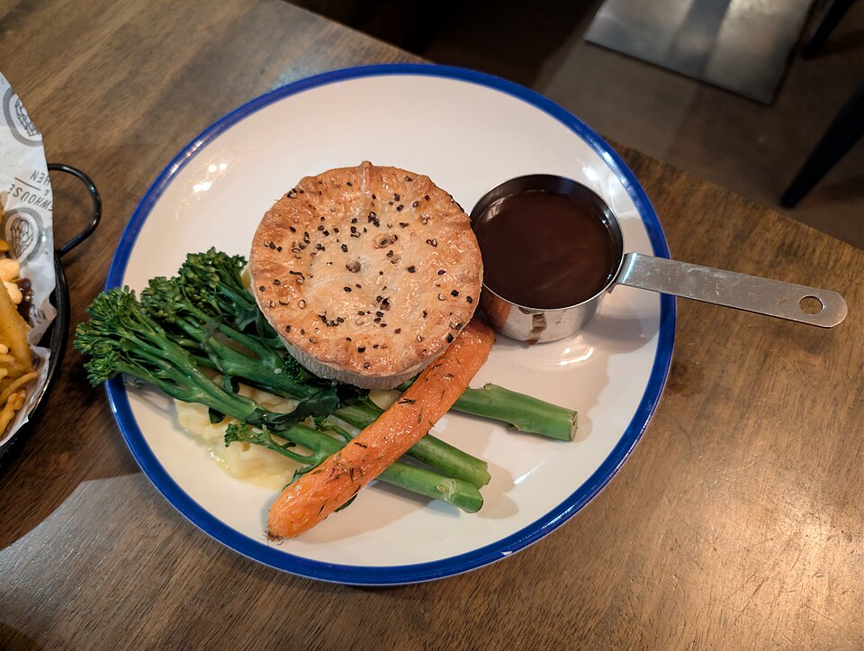 A steak and ale pie served with gravy, broccoli and carrot