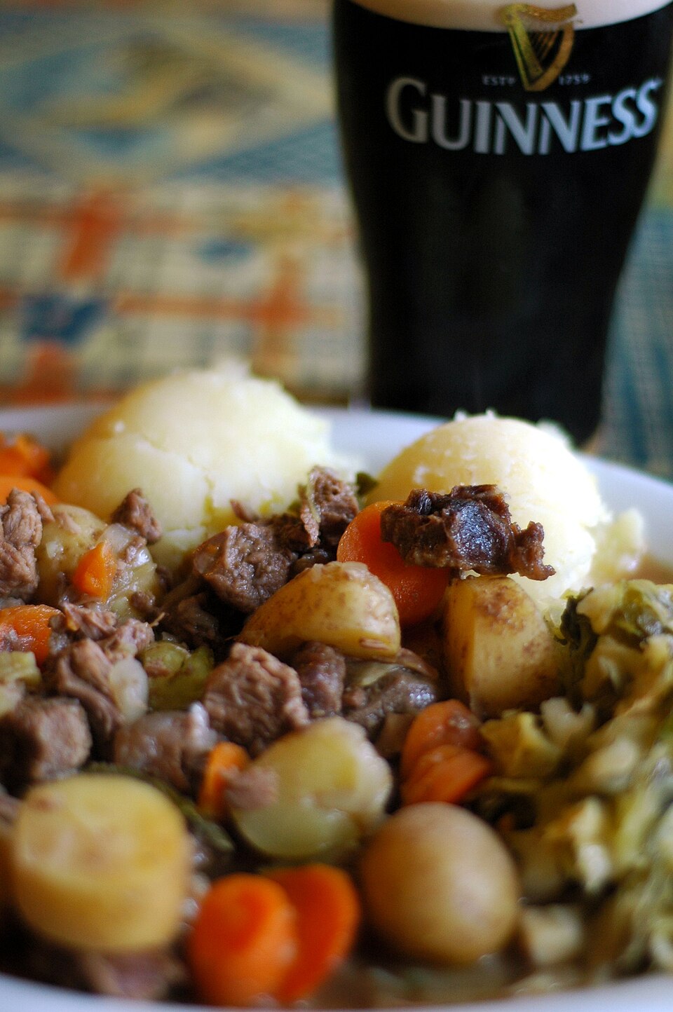A bowl of Irish beef stew with potatoes, beside a pint of Guinness