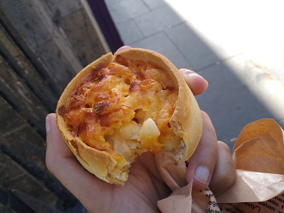 A macaroni pie in a hot-water-crust pastry case, held in the hand