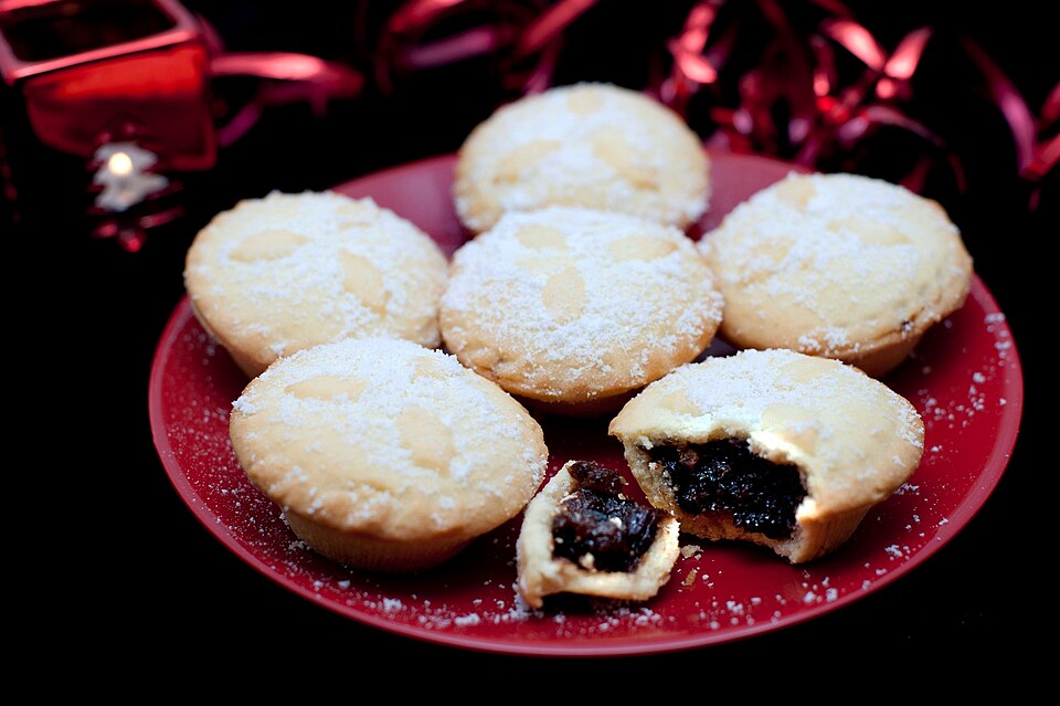 A plate of sugar-dusted mince pies, one cut open