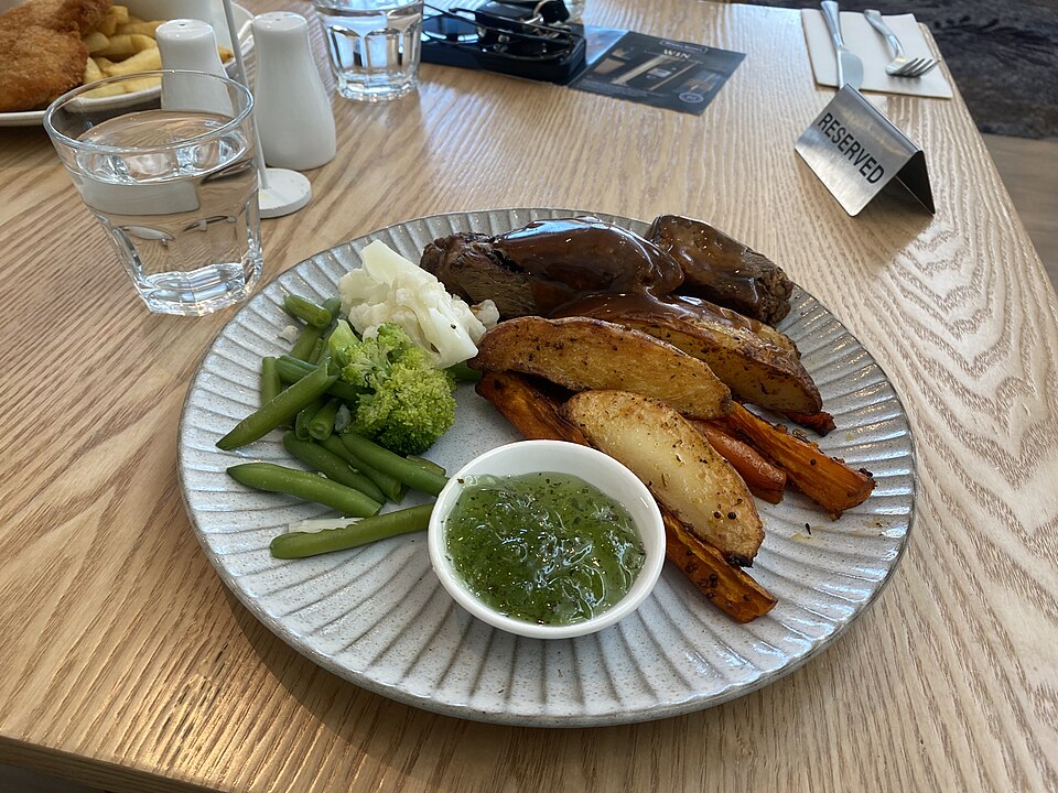 Slices of roast lamb with roast potatoes, green vegetables and mint sauce