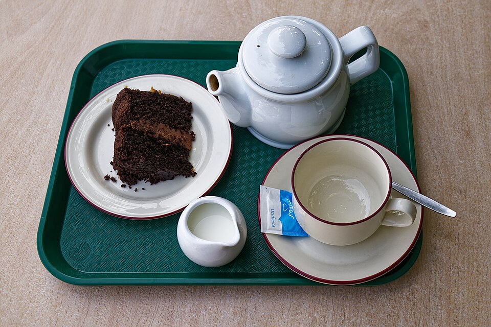 A tea tray with a teapot, cup, milk jug and slice of cake