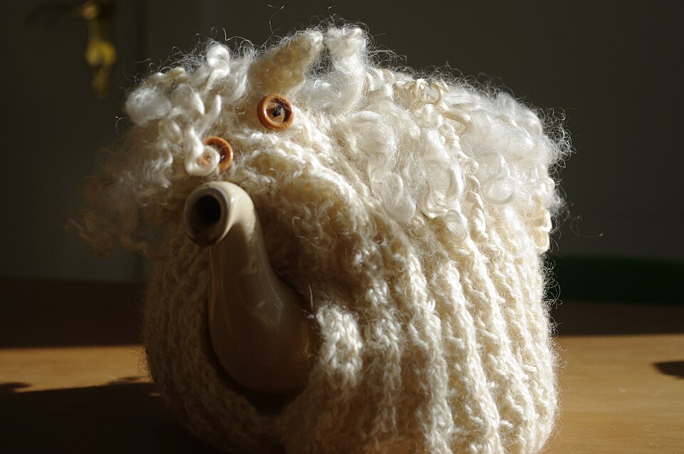 A teapot wearing a knitted tea cosy shaped like a sheep